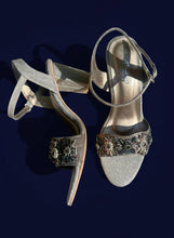 Load image into Gallery viewer, Pair of glittery high-heeled shoes with decorative straps on a concrete surface