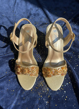Load image into Gallery viewer, Gold high-heeled sandals with embellishments on a metallic surface