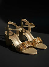 Load image into Gallery viewer, Gold glittery shoes with decorative straps on a textured surface