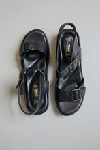 Load image into Gallery viewer, Pair of black sandals with buckles on a beige surface