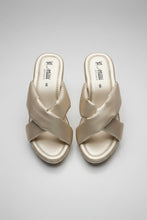 Load image into Gallery viewer, A pair of women's slide sandals with wide, crisscrossed straps in a light champagne-gold satin fabric, resting on a gray textured surface. The insoles show the brand name 'mmi'.