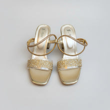 Load image into Gallery viewer, Pair of gold sandals with clear soles on a gray surface
