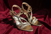 Load image into Gallery viewer, Pair of gold and silver strappy sandals on a reflective surface