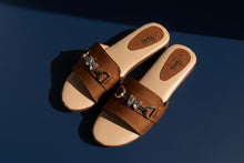 Load image into Gallery viewer, Pair of brown sandals with metallic buckles on a concrete surface