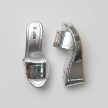 Load image into Gallery viewer, A pair of metallic silver platform mule sandals with a buckle strap, displayed on a textured gray stone surface. The insole shows the brand name 'mwi' and size '7'.