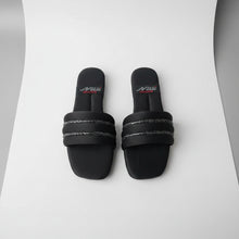 Load image into Gallery viewer, Pair of black slides with 'New' branding on a gray floor.
