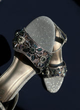 Load image into Gallery viewer, Silver high-heeled shoe with decorative embellishments on a textured surface
