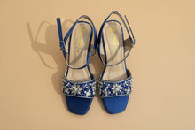 Load image into Gallery viewer, Pair of blue high-heeled shoes with floral embellishments on a gray surface
