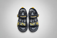 Load image into Gallery viewer, Black sandals with yellow accents on a gray surface
