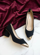 Load image into Gallery viewer, Black high-heeled shoes with gold tips on a gray concrete surface
