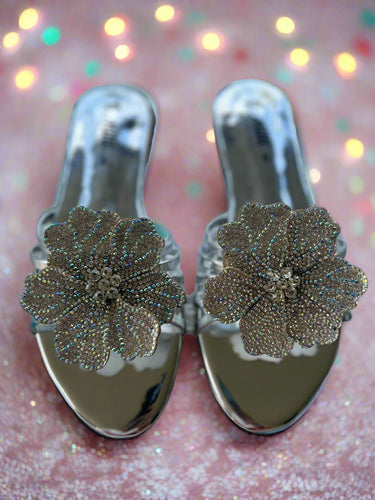 Pair of silver shoes with floral embellishments on a textured surface