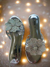Load image into Gallery viewer, Pair of silver high-heeled shoes with floral embellishments on a textured surface
