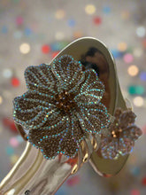 Load image into Gallery viewer, Gold sandal with a decorative flower embellishment on a textured white background
