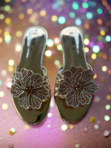 Gold sandals with floral embellishments on a textured white surface