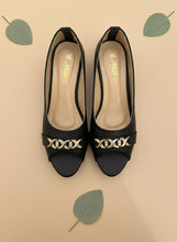 Load image into Gallery viewer, Black high-heeled shoes with gold embellishments on a blue background
