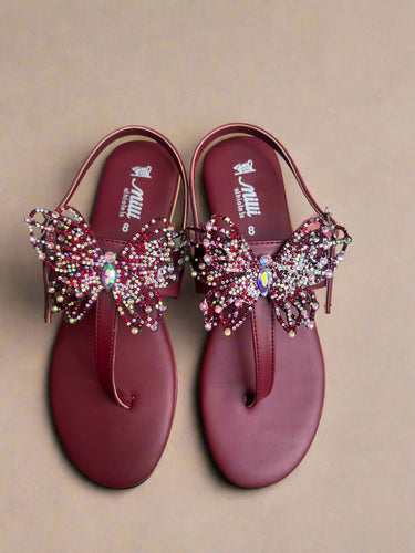 Maroon sandals with decorative embellishments on a gray surface