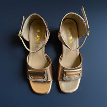 Load image into Gallery viewer, Pair of gold high-heeled shoes with a strap on a gray surface
