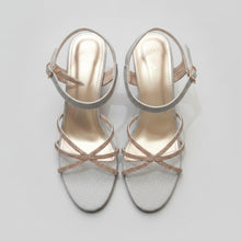Load image into Gallery viewer, Pair of silver high-heeled sandals with gold straps on a gray surface
