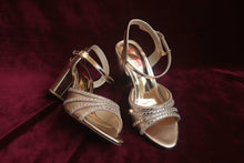 Load image into Gallery viewer, Pair of gold high-heeled shoes with embellishments on a gray surface

