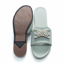 Load image into Gallery viewer, A pair of women's slide sandals in a textured pale sage green fabric, shown from both the top and the sole. The top features a wide strap adorned with a decorative bow embellished with rhinestones.
