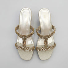Load image into Gallery viewer, Pair of silver high-heeled sandals with gold embellishments on a gray marble surface.
