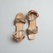 Load image into Gallery viewer, Pair of gold high-heeled sandals with decorative bows on a gray surface
