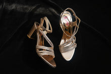 Load image into Gallery viewer, Pair of gold high-heeled shoes on a gray concrete surface
