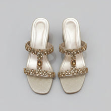 Load image into Gallery viewer, Pair of silver high-heeled sandals with gold embellishments on a gray surface
