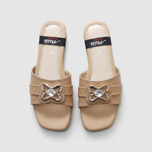 Load image into Gallery viewer, A pair of beige slide sandals with decorative metallic bow-shaped embellishments set with clear rhinestones, shown on a gray stone-textured background. The insoles feature a black band with the brand name 'mm' and 'SHOES' printed on it.
