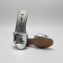 Load image into Gallery viewer, A pair of metallic silver slide sandals with a glossy finish, featuring a wide strap and a square buckle detail, resting on a dark textured surface.
