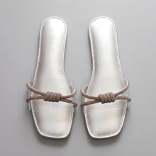 Load image into Gallery viewer, A pair of women's square-toe slide sandals with metallic silver insoles and brown knotted elastic straps, displayed on a dark gray marble surface.
