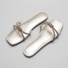 Load image into Gallery viewer, A pair of women's flat sandals with square toes, featuring a metallic champagne pink footbed and a textured metallic rose gold woven strap with a knotted detail, displayed on a gray marble surface.
