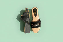 Load image into Gallery viewer, Black sandal with decorative strap and heart detail on a textured surface
