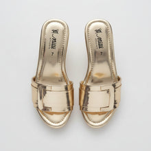 Load image into Gallery viewer, A pair of metallic rose gold slide sandals with wide straps and a square buckle detail, shown on a gray textured surface. The brand name 'Mimi' is visible on the insoles.
