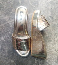 Load image into Gallery viewer, A pair of metallic silver platform slide sandals with buckle straps, displayed on a gray stone-textured surface.
